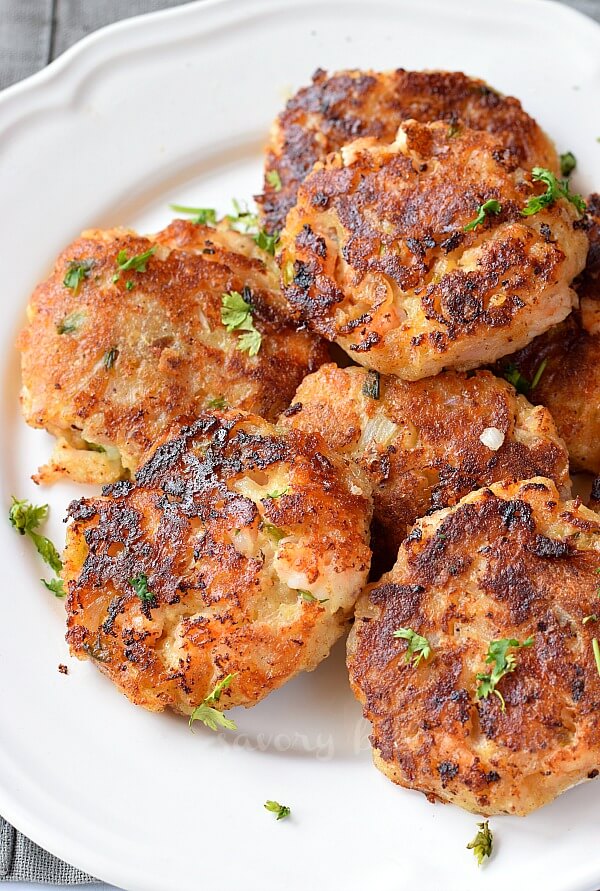 a white plate with stacked shrimp cakes with chopped cilantro