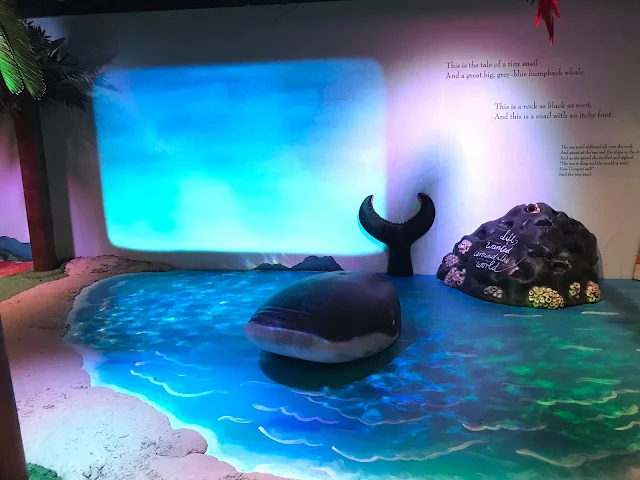 A whale model in a painted sea next to a rock with some writing on
