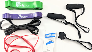 A birds eye view of the Polygon Resistance Bands Set. There are four bands, two handles, the workout guide, and one door anchor.
