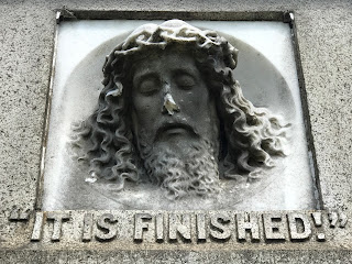 Photo of a carving of the head of Jesus in the top centre of a gravestone.  His nose is chipped.  “It is finished.” Hear him cry, Learn of Jesus Christ to die. Burial place of Isaac and Mary Blackwood. Photo by Kevin Nosferatu for The Skulferatu Project.