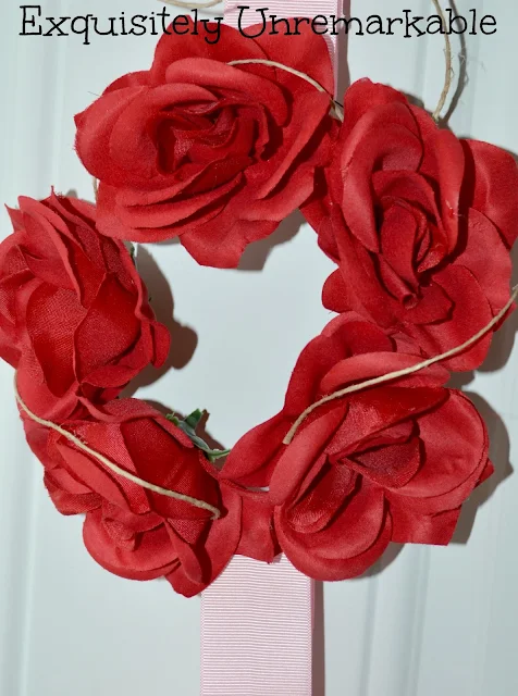 Red rose wreath with twine and pink ribbon on door