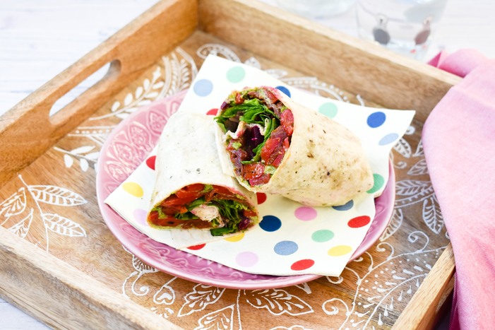 Vegan Red Pepper & Kale Lunch Wrap on a spotted white napkin, on a pink tea plate sitting on a wooden tray