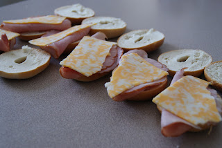 Mini bagels sandwiches, sliced and topped with ham and cheese slices.