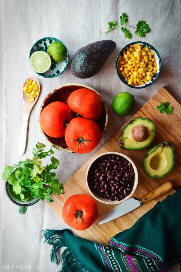 INGREDIENTES PARA TOMATES RELLENOS TEXMEX, FRIJOLES, AGUACATE, TOMATES, MAÍZ, CILANTRO, LIMA, SOBRE TABLA MADERA CORTAR, MANTEL LINO BEIGE