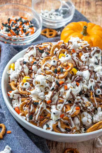 White bowl with popcorn, candy, sprinkles covered in chocolate drizzle.