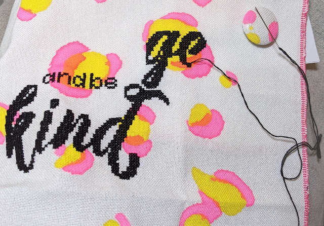 work in progress photo of black cross stitch word being stitched on hand printed yellow and pink leopard spot fabric