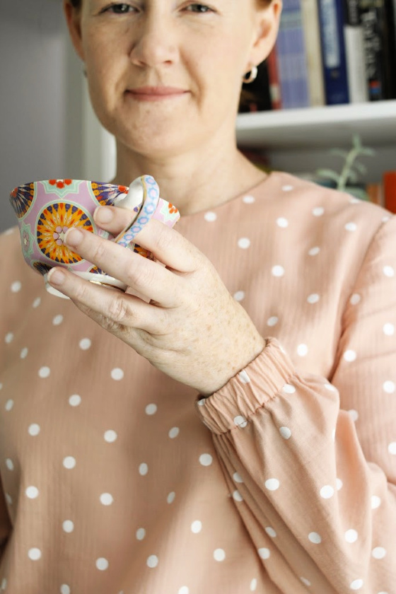 photo of a woman holding a tea cup and showing the cuffs of a long sleeved top