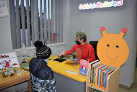 Bibliotekarka ubrana w czapkę Mikołaja wypożycza dziecku książki w Oddziale dla Dzieci Biblioteki w Zelowie.