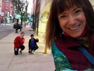 A selfie of my face with 2 friends in the background - along with a chalked sidewalk that reads "Mile 10,000."