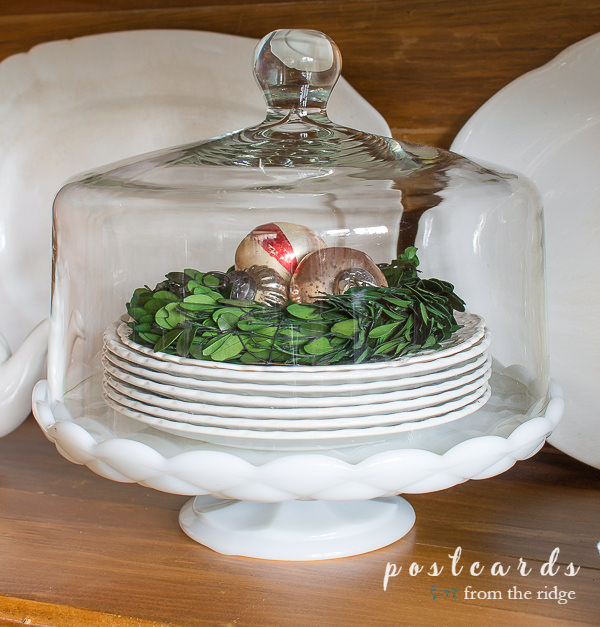 cake stand with white plates, small green wreath, and Christmas ornaments