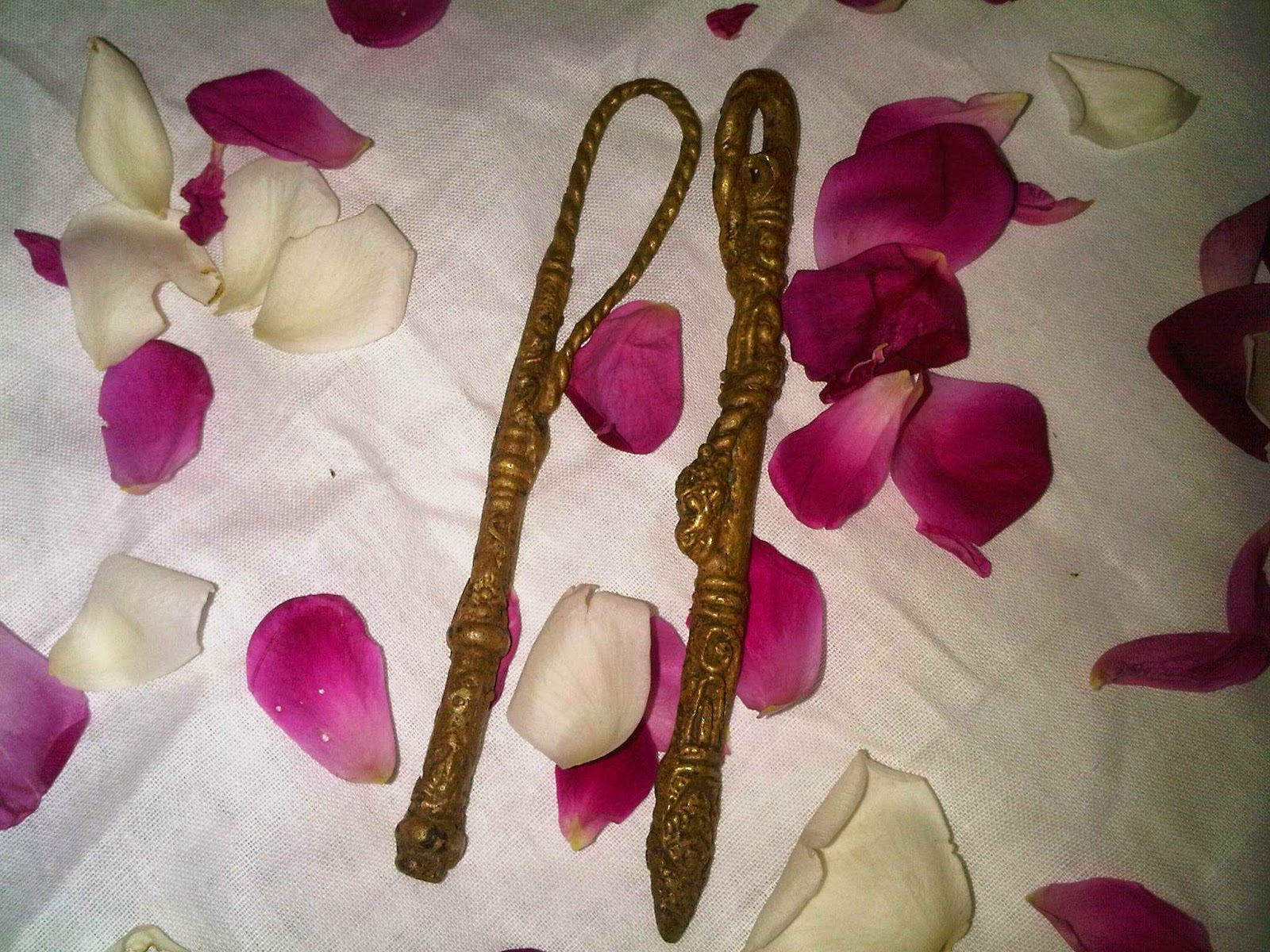  A pair of heirloom objects with negative energy made of bronze and decorated with a lion's head, laying on a white cloth with pink and white rose petals scattered around them.