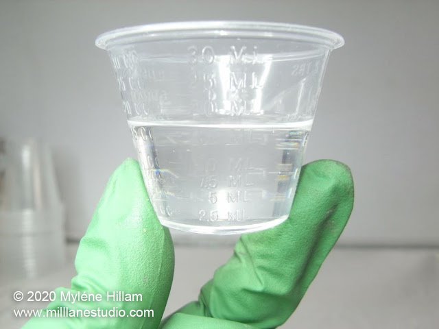 Gloved hand holding a small plastic cup filled with clear, bubble-free resin