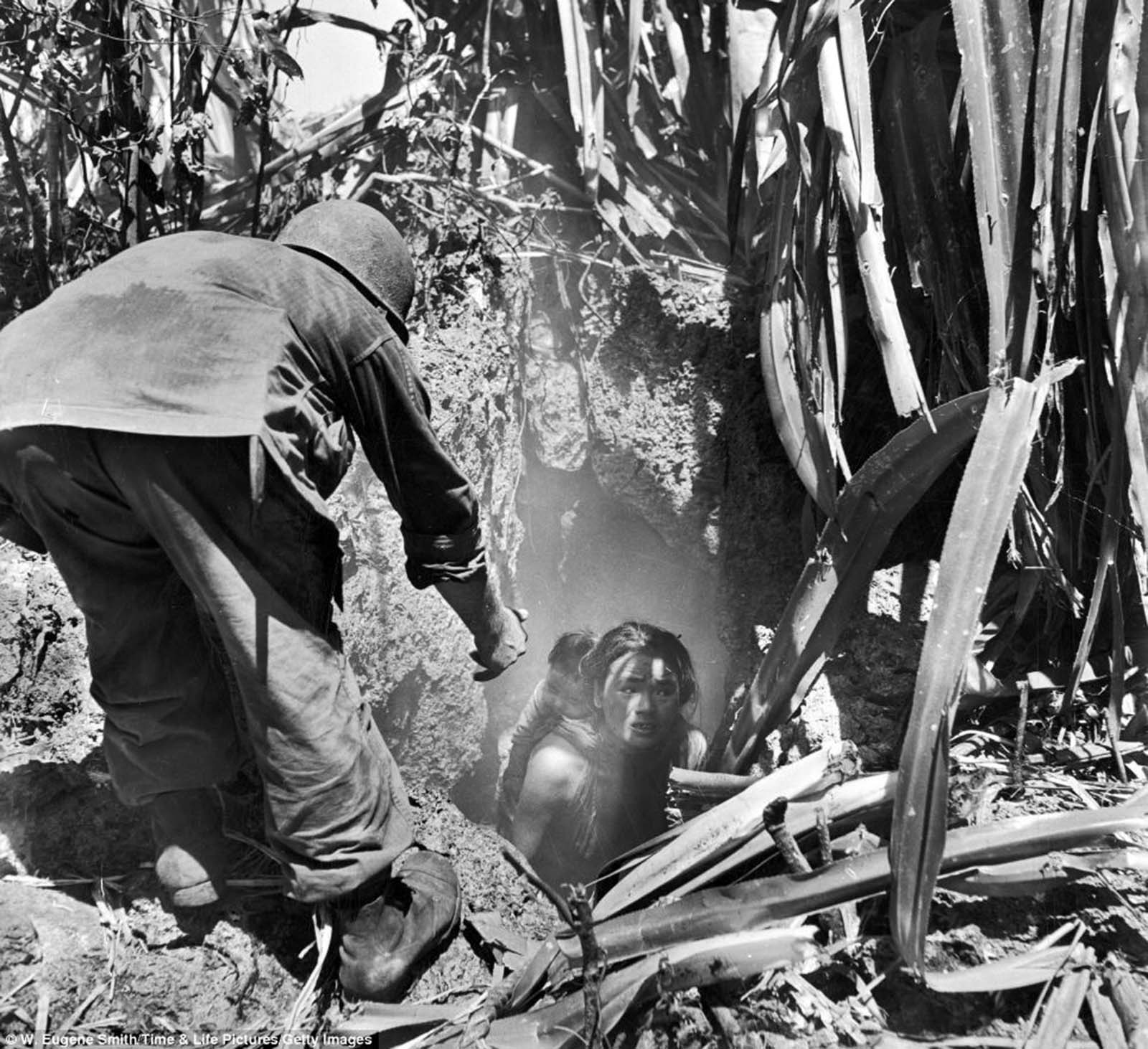 A US soldier offers his hand to a woman leaving a cave where she had hidden with her child during the battle between Japanese and American forces. Saipan, 1944