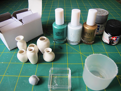 Slection of dolls' house miniature white vases, bottles of nail varnish and paint and plastic containers on a cutting mat.