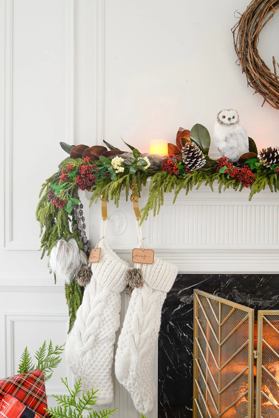 a faux christmas fireplace mantel garland with red seeded eucalyptus, a cedar garland and magnolia leaves. A galvanized bucket holding christmas gifts