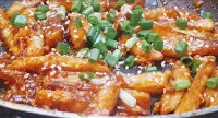Honey chilli potato recipe topped with green scallions and white sesame seeds