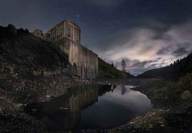 Infraestructura abandonada de una mina de carbon reflejada en una charca bajo un cielo nocturno