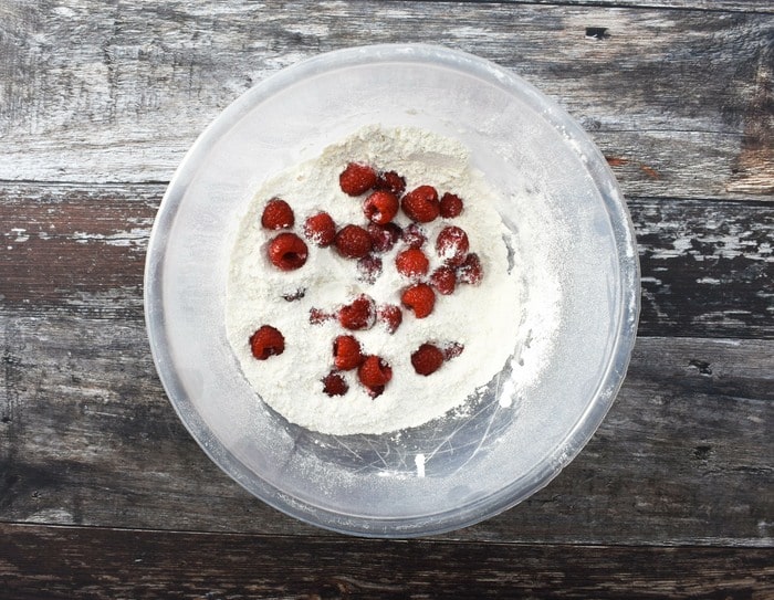 flour in a mixing bowl topped with raspberries