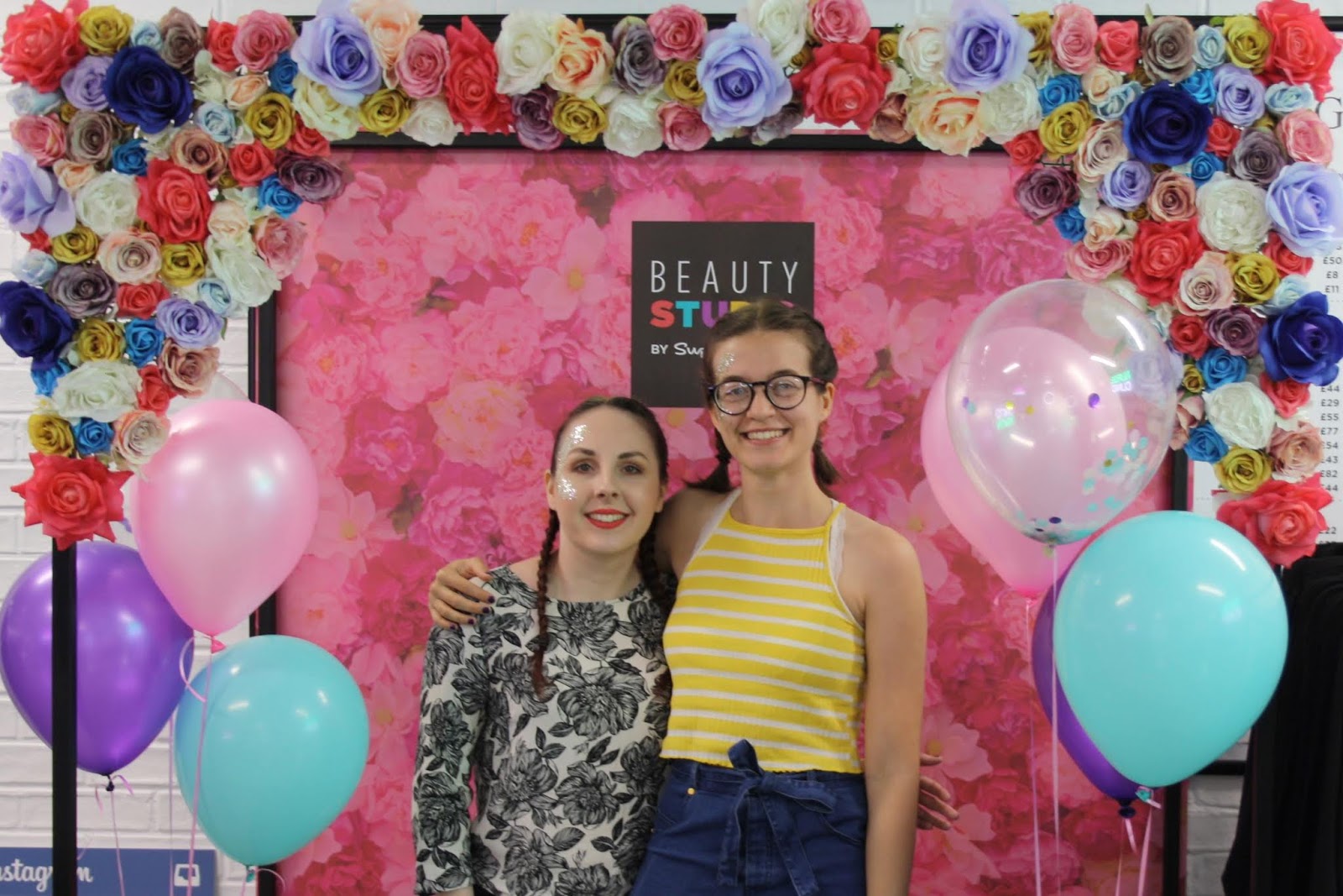 Abbey and Kirstie stand in front of a floral photo booth