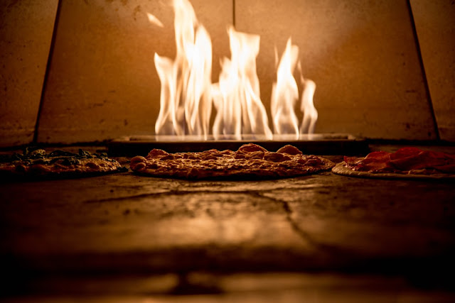 A picture of a wood-fired oven with pizzas cooking inside it 