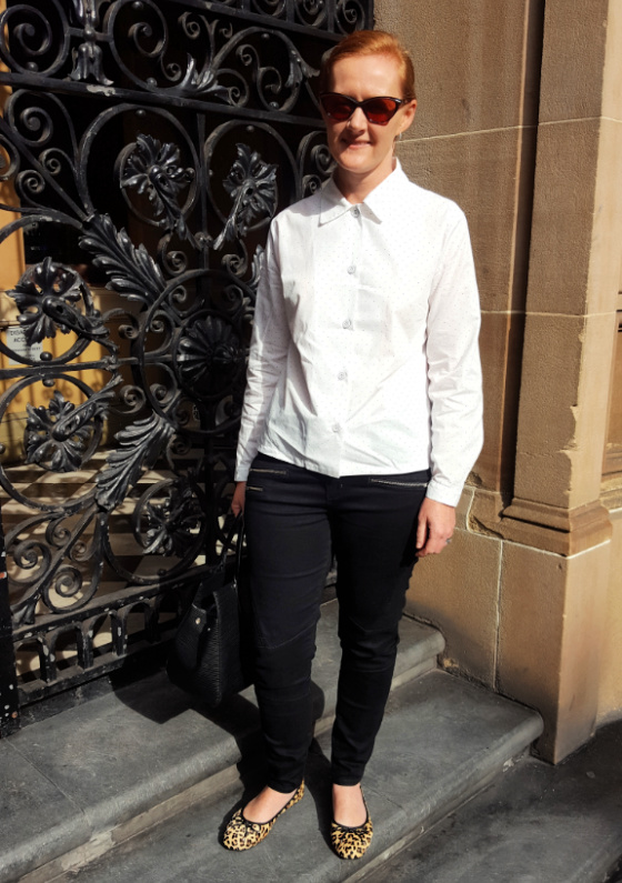 a lady wearing black jeans and a white shirt standing in front of a wrought iron door