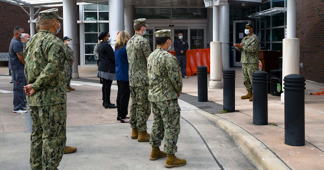 A group of people in uniform, spaced 6 feet apart from each other, in front of a building.