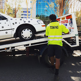 White car with black daisies on it being mounted onto a tow truck.