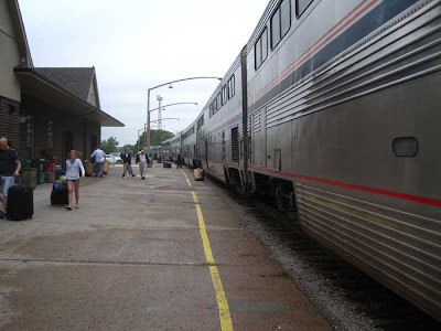 Silver Amtrak train with red, white and blue stripes at a train station