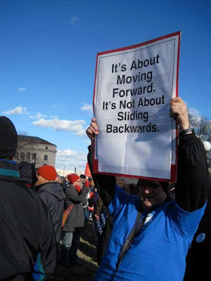Man with sign reading It's about moving forward, not sliding backward