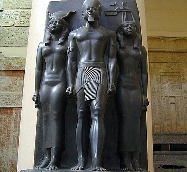 Повязка "шендит" на царе, классические длинные платья на богинях. Скульптурная группа царя Менкаура с Хатхор и покровительницей нома. Граувакка. 25 в. до н.э. Каир, Египетский музей
