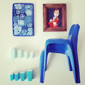Flat lay of one-twelfth modern miniature items in blue and white, including a painted portrait, a wall piece, a Sebel plastic chair, and retro kitchen containers