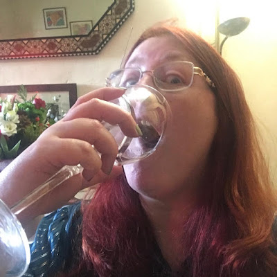 A redheaded woman gulping a glass of wine