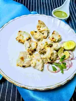 Serving Chicken malai tikka in a plate with onion and lemon wedges,green chutney in background