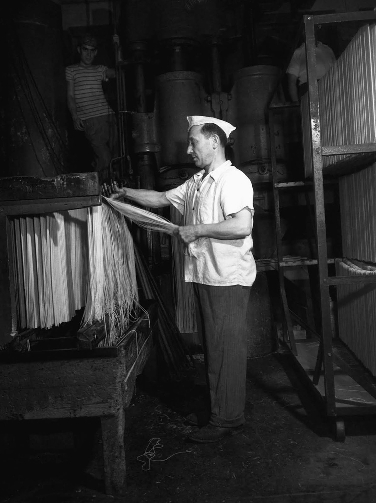 A worker for Atlantic Macaroni Company hangs spaghetti to dry at a factory in Long Island City, New York. 1943.