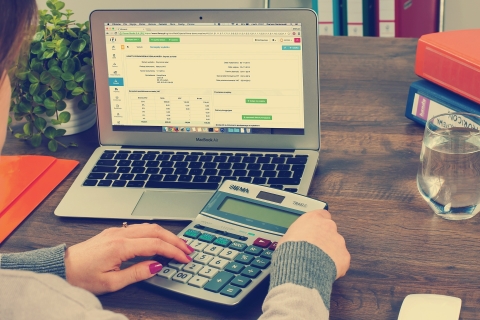 Image of Person Filing Tax Return with Calculator and Laptop