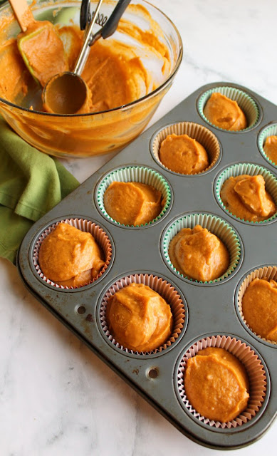 scratch made pumpkin cupcake batter scooped into cupcake liners with mixing bowl and cookie scoops in background