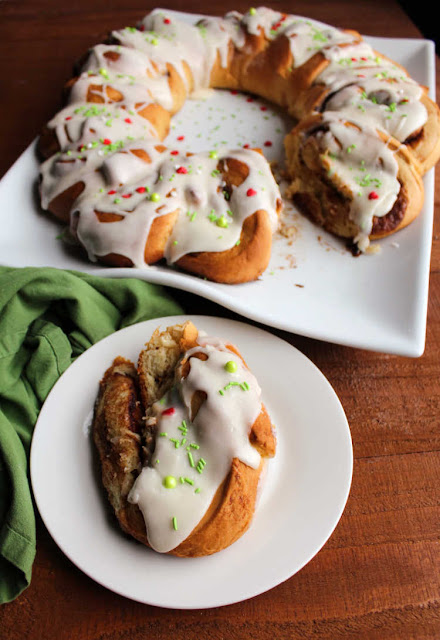 Soft and sweet cinnamon rolls take on a festive wreath shape. They are a perfect holiday breakfast or something fabulous for overnight guests. iced cinnamon roll on plate with remaining wreath in background