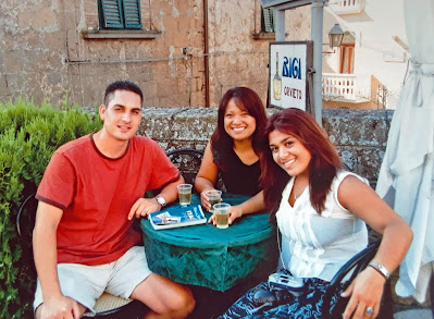 man and two women seated at a table outdoors with plastic cups of white wine