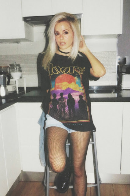 Estilo grunge con camiseta negra ancha con imagen del grupo The Doors, pantalón corto, medias de red pequeña, botas estilo militar y cazadora vaquera