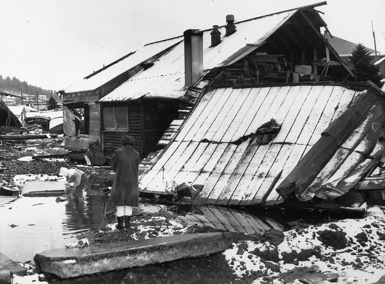 Egy anya figyel, miközben gyermeke egy vízcseppekben játszik, az 1964 márciusában az alaszkai Kodiakban, földrengés rombolt otthonában. 