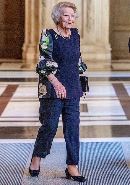 Princess Beatrix of the Netherlands wore a navy blue floral tulip print blouse, and navy blue trousers. Gold necklace