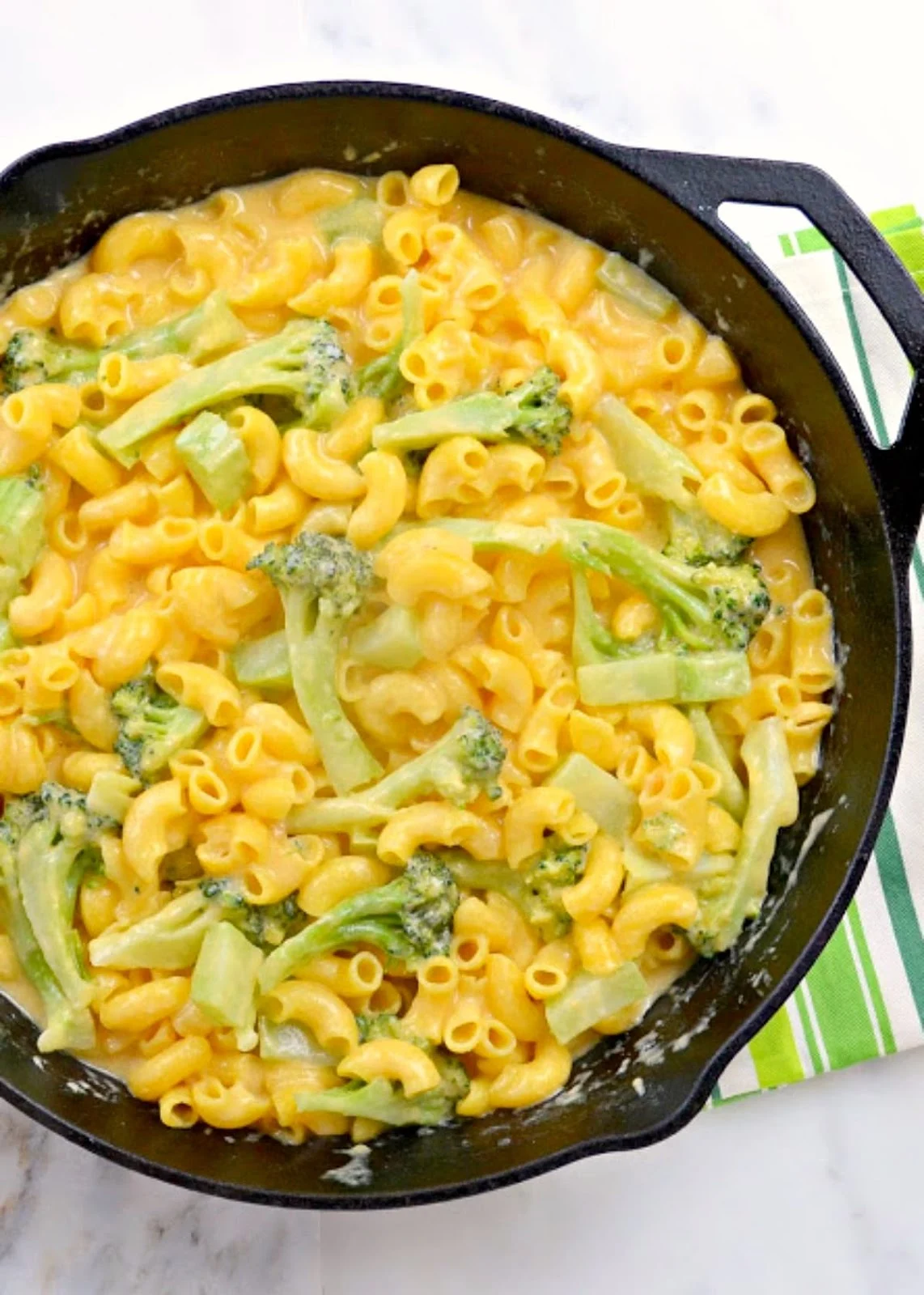 Creamy Macaroni and Cheese with Broccoli in a cast iron skillet with a green and white striped hand towel.