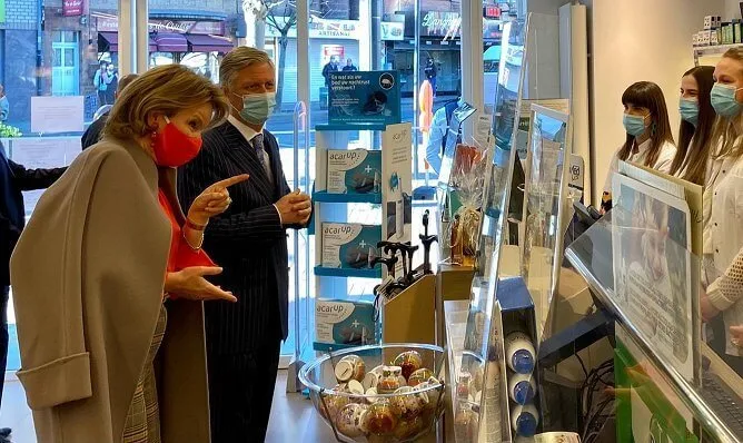 Queen Mathilde wore an orange color silk top and mask from Natan, and a beige wool coat by Natan. the pharmacy Pharma Haelvoet in Evere