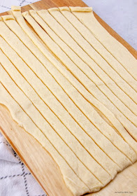 Cutting board with crescent rolls spread out and sliced in small strips