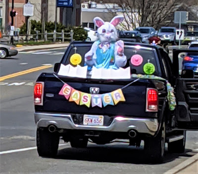 A person in an Easter Bunny costume sits on a chair in the back of a black pick-up truck with decorations around it celebrating Easter.