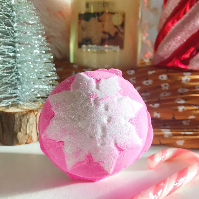 Lush Snow Fairy bath bomb in front of silver christmas tree, home bargains candle and red and white swirl ornament