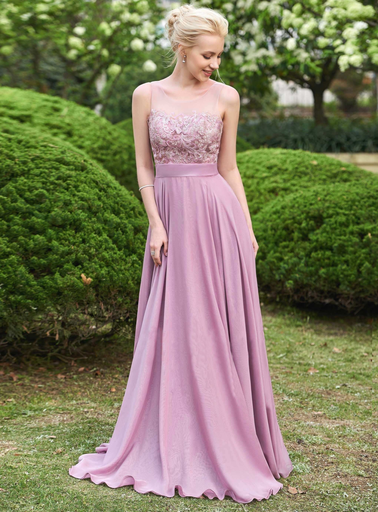 a beautiful bridesmaid in a long, pink dress is posing on a green grass