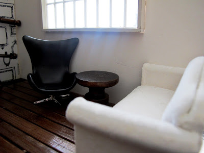 Modern dolls' house miniature room corner with a white sofa, black egg chair and a wooden side table.