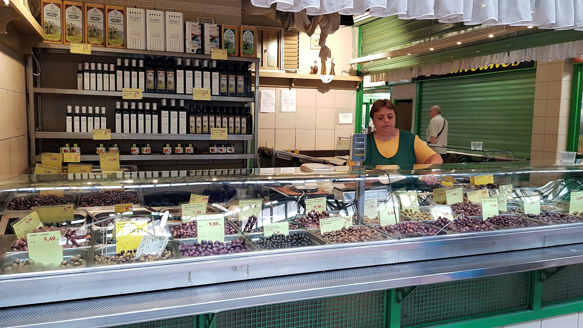 A food stall selling olives and a woman seller in a green apron