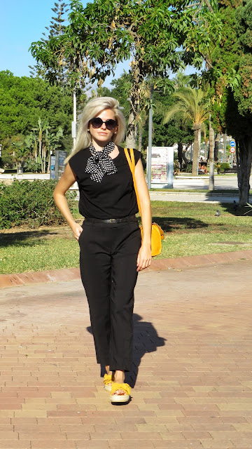 Alejandra Colomera con camiseta negra, pantalón formal negro, lazo en el cuello negro con lunares blancos y complementos mostaza